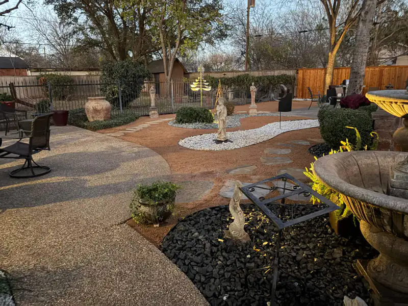 Backyard patio with a stone fountain, black river rock and a white rock pathway