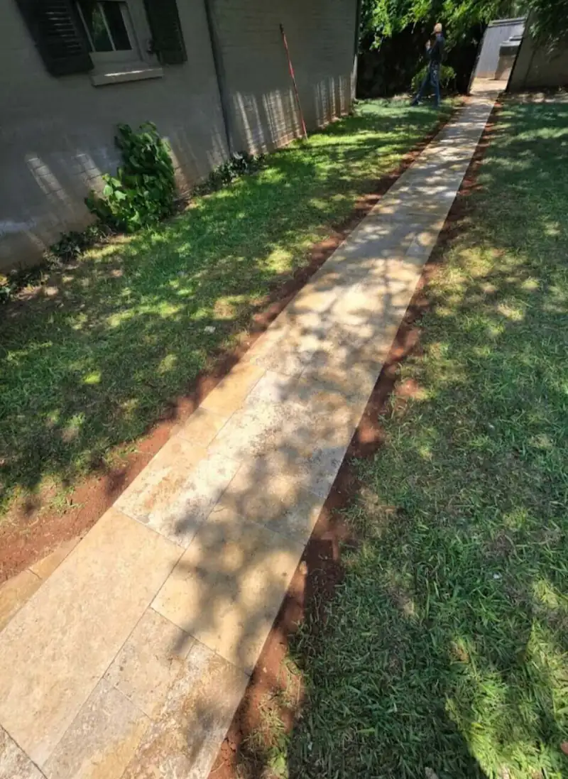 Long limestone flagstone walkway along the side of a house through dappled shade