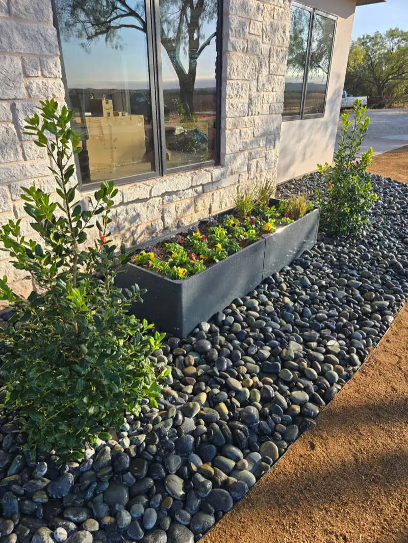 River rock bed with steel planters and native shrubs along a limestone home in Abilene, TX
